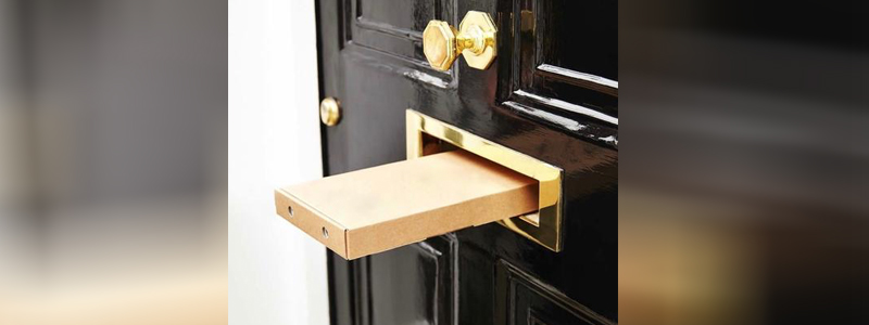 slim brown cardboard box being delivered through a letterbox in a front door